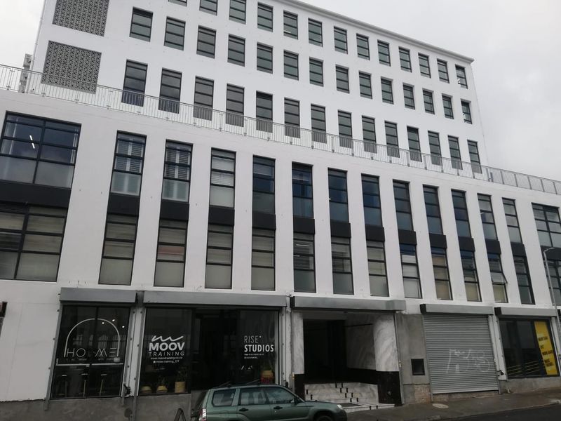 A multi-story commercial office building facade featuring large windows, ground-level retail access, and a prominent entrance with stone steps.
