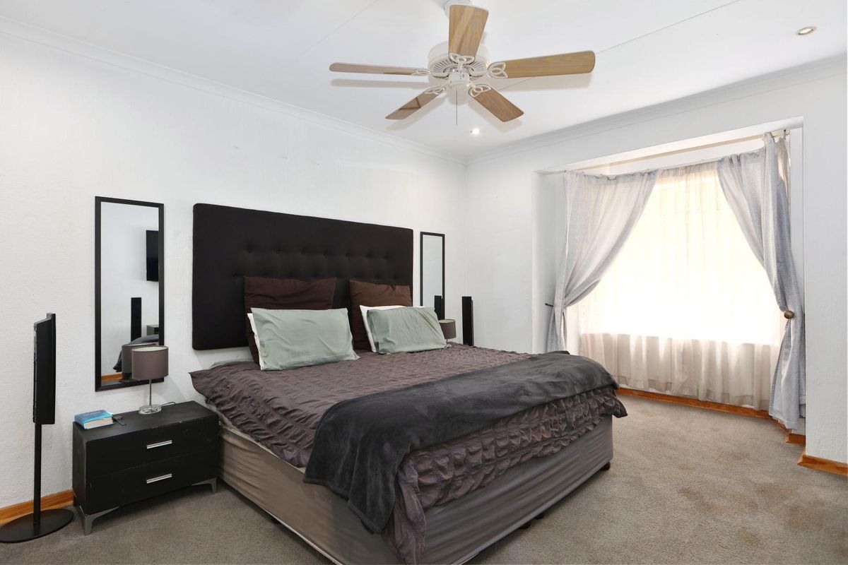 A spacious bedroom featuring a ceiling fan, neutral wall finishes, and large windows allowing for natural light.