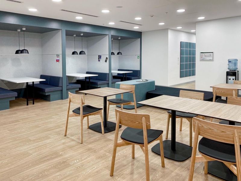 Modern open-plan office breakout area featuring built-in booth seating, recessed ceiling lights, and durable wood-look flooring in a clean, professional environment.