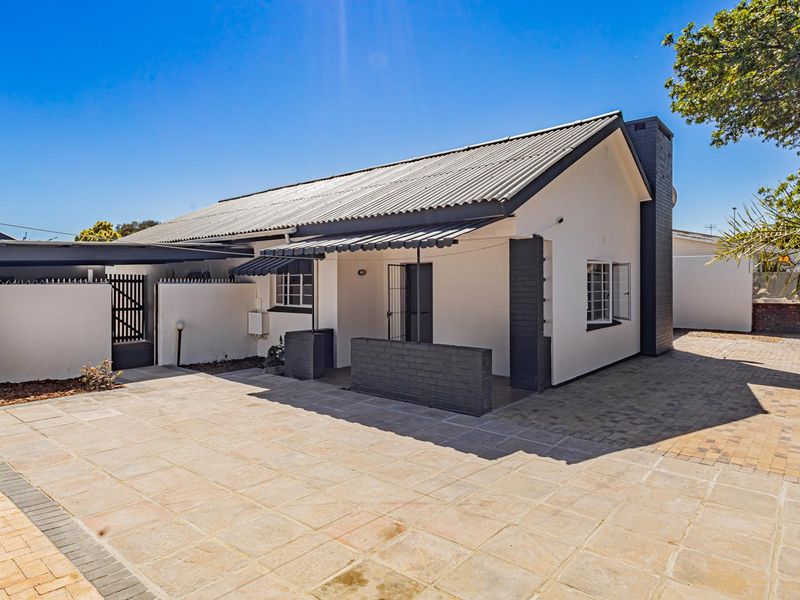 Front exterior view of a well-maintained house featuring a paved driveway, covered patio area, and secure perimeter fencing.