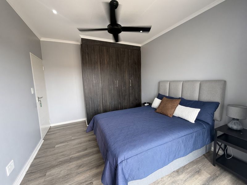 A well-maintained bedroom featuring dark wood built-in cupboards, modern laminate flooring, and a ceiling fan, offering a clean and contemporary living space.