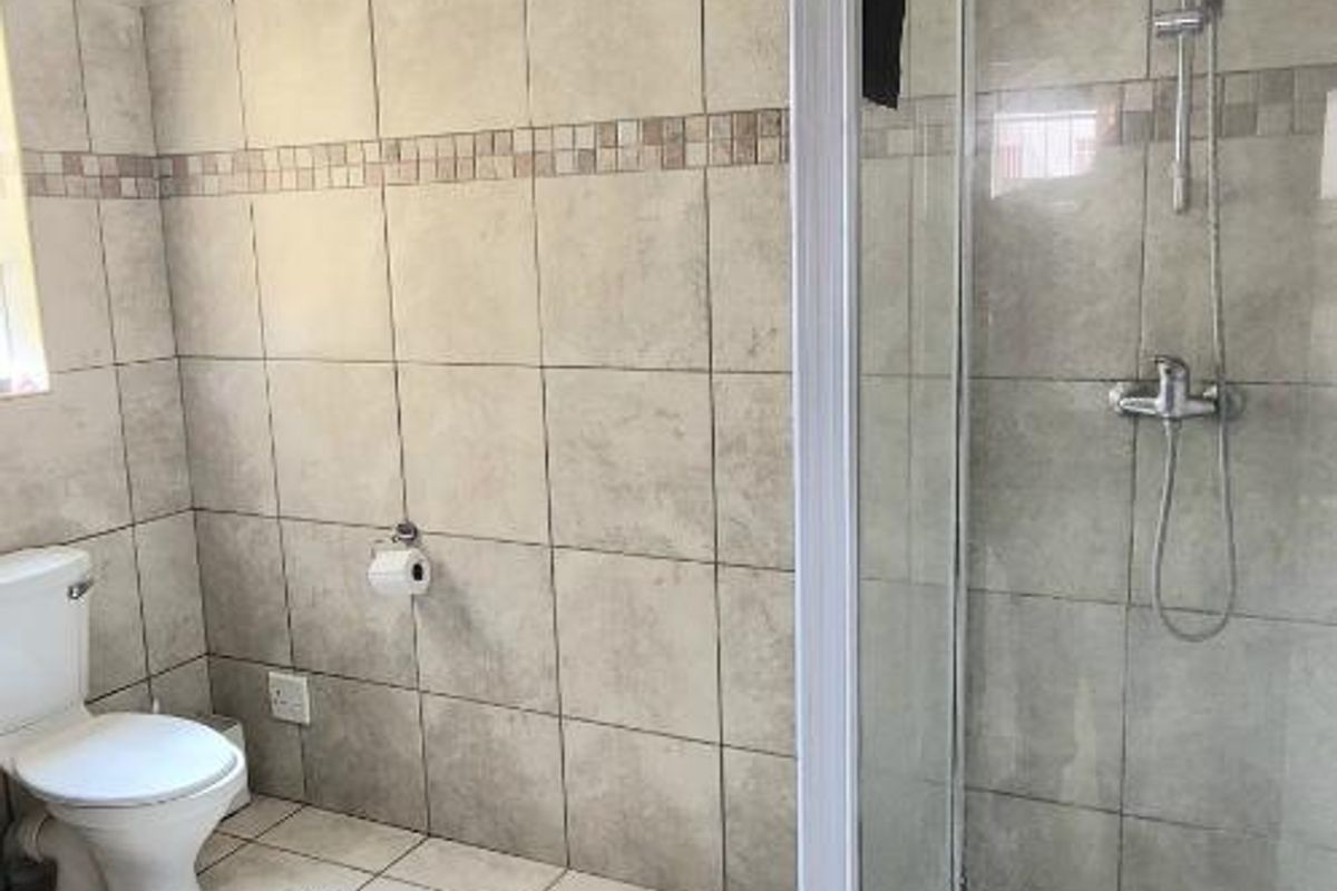 A functional bathroom featuring a glass-enclosed shower, ceramic wall and floor tiling, and a standard toilet.