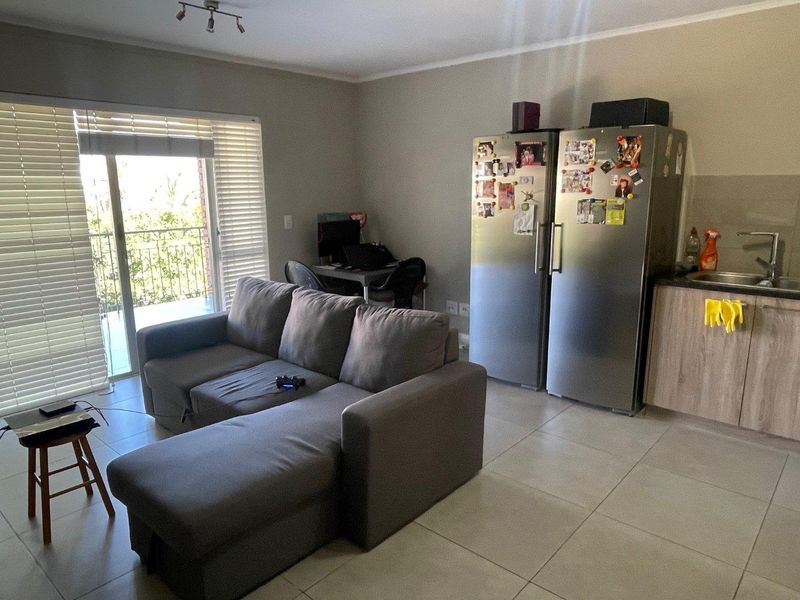 Open-plan living area featuring tiled floors, a compact kitchen section with cabinetry and sink, and a sliding door leading to a balcony.
