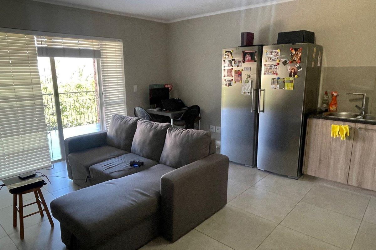 Open-plan living area featuring tiled floors, a compact kitchen section with cabinetry and sink, and a sliding door leading to a balcony.