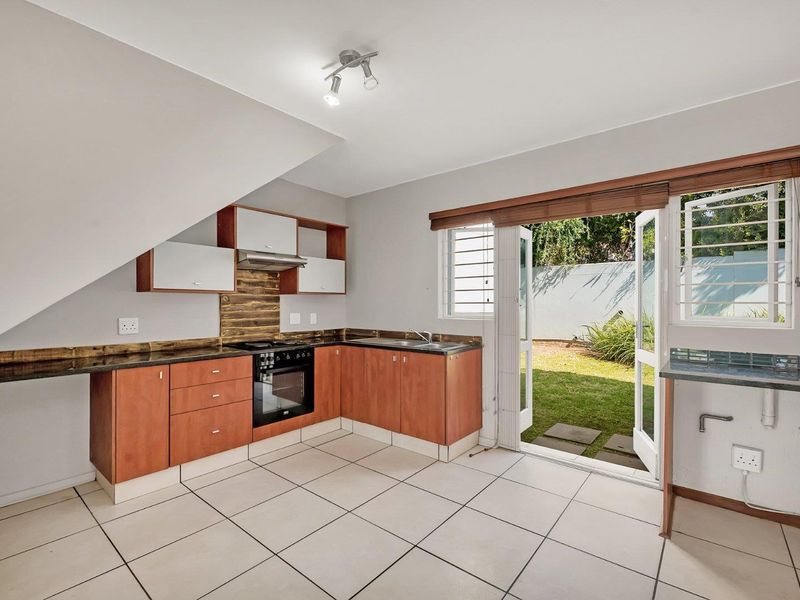 A functional kitchen featuring built-in cabinetry, granite countertops, and integrated appliances, with direct access to a private garden through glass french doors.