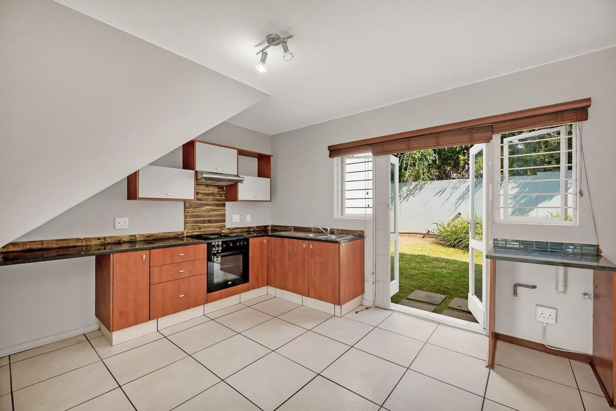 A functional kitchen featuring built-in cabinetry, granite countertops, and integrated appliances, with direct access to a private garden through glass french doors.