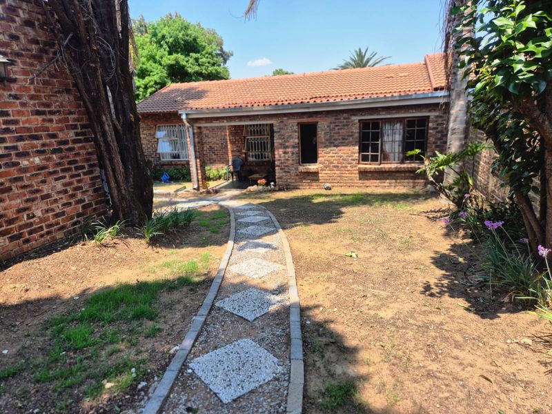 Rear view of a brick townhouse featuring a tiled roof, security-fitted windows, and a decorative paved garden path leading to the entrance.