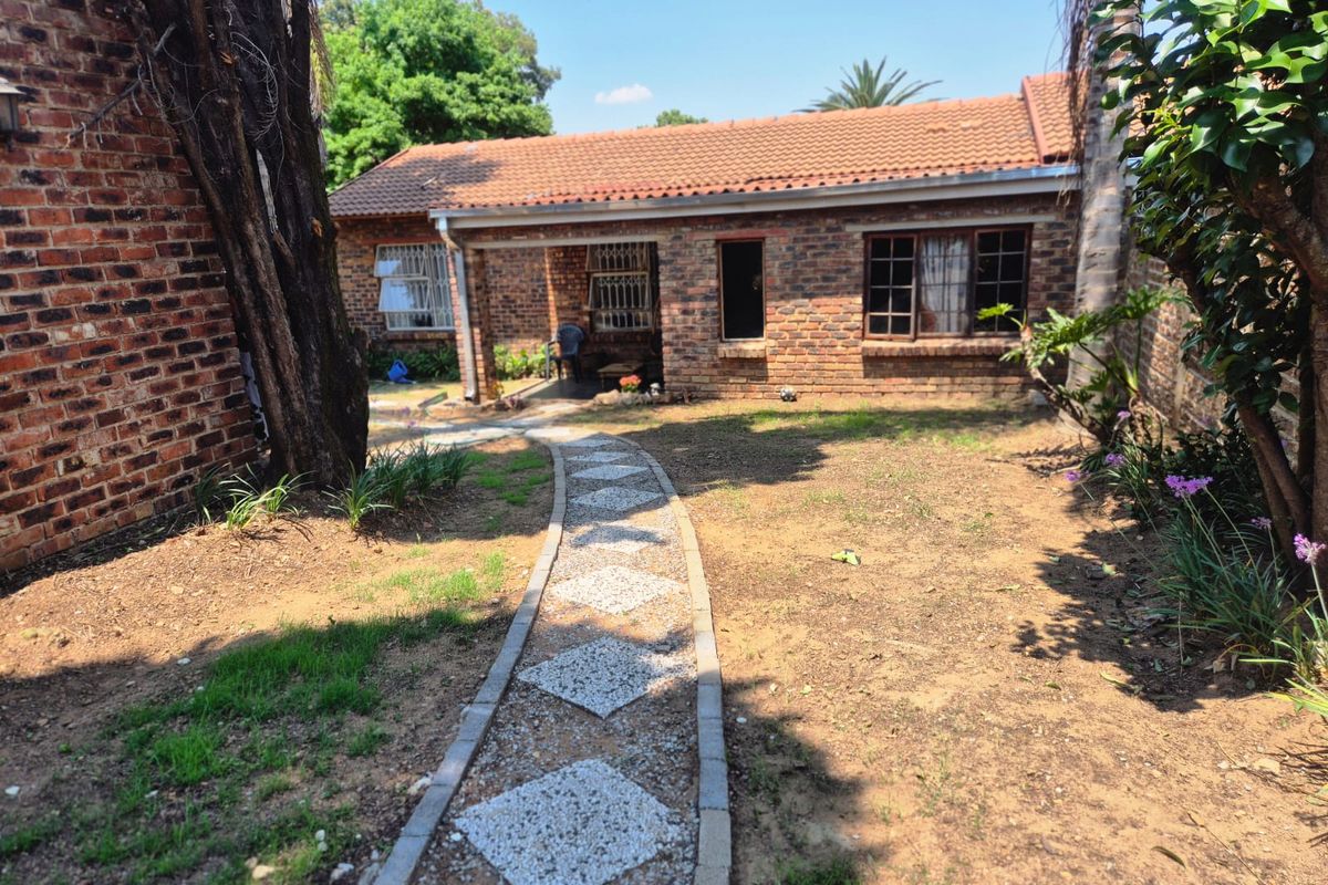 Rear view of a brick townhouse featuring a tiled roof, security-fitted windows, and a decorative paved garden path leading to the entrance.