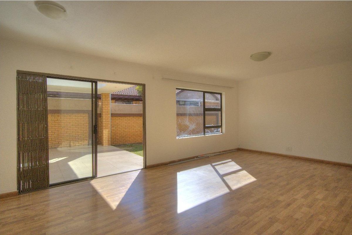 Spacious, empty living area featuring laminate flooring, large windows, and a sliding glass door providing direct access to the outdoor patio area.