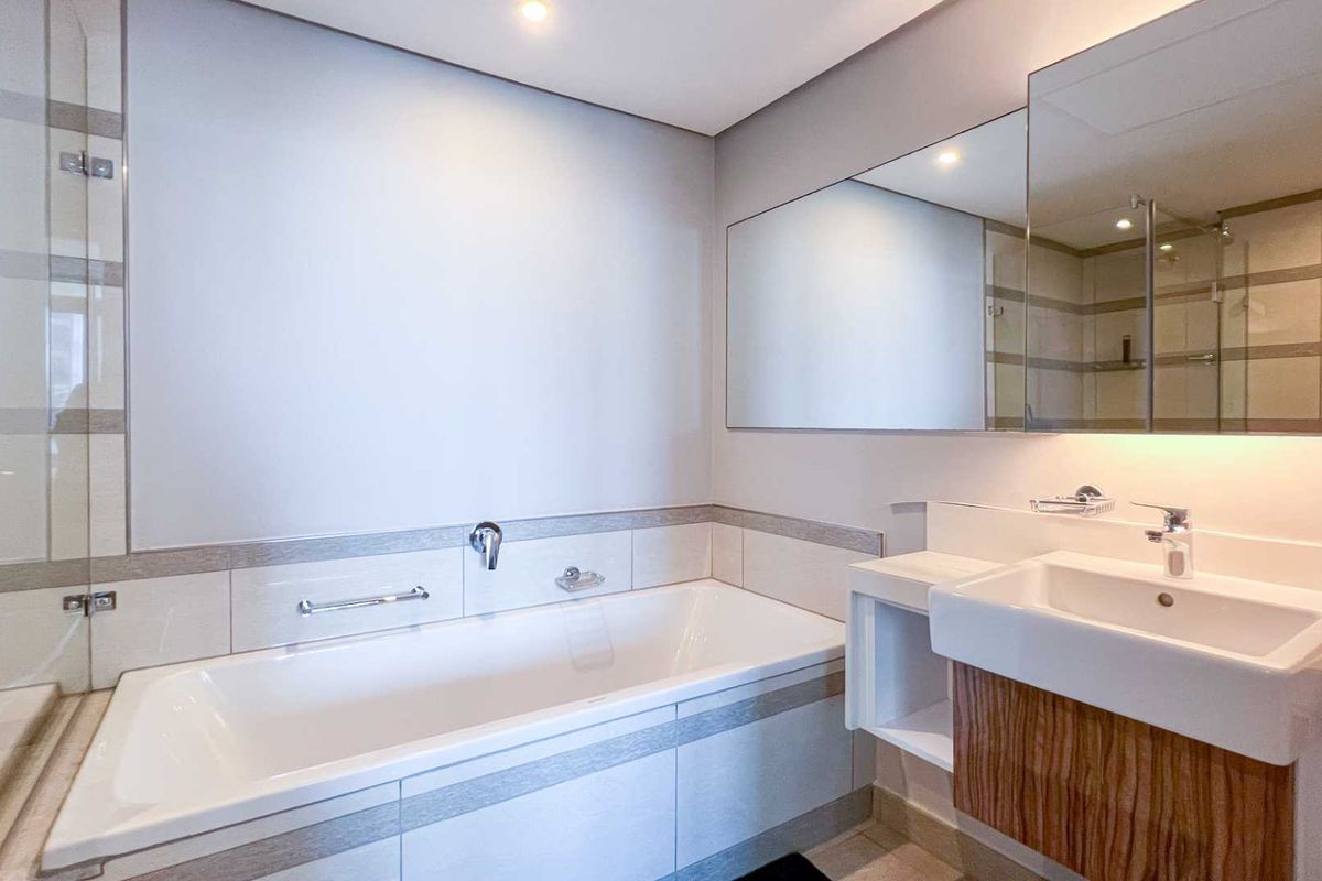 Modern bathroom featuring a built-in bathtub, wall-mounted basin with wooden vanity cabinet, and large wall-to-wall mirror.