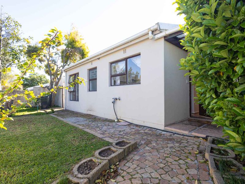 Rear exterior view of the property featuring a paved walkway, established garden, and access to the home via a side entrance.