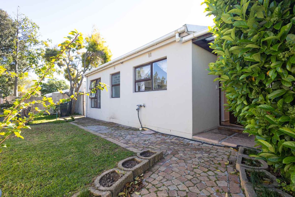 Rear exterior view of the property featuring a paved walkway, established garden, and access to the home via a side entrance.