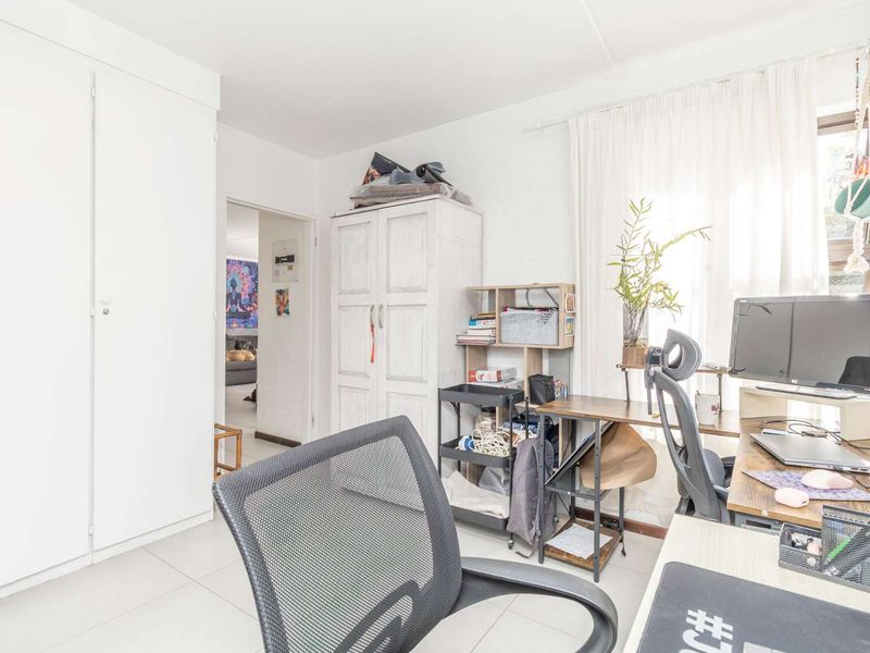 A functional bedroom featuring built-in cupboards and neutral tiled flooring, currently utilized as a home office space.