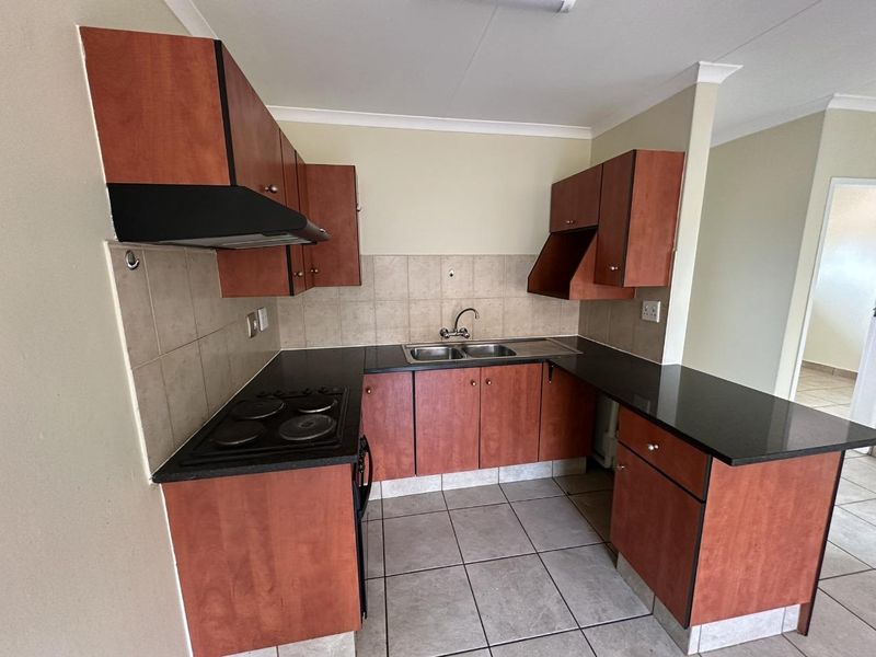 A functional kitchen featuring laminate cabinetry, granite countertops, a double bowl sink, and an integrated electric hob with an extractor fan.