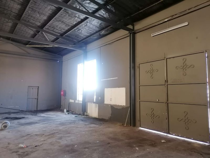 Spacious industrial utility area featuring exposed steel roof trusses, concrete flooring, and a large metal access door, suitable for storage or workshop use.