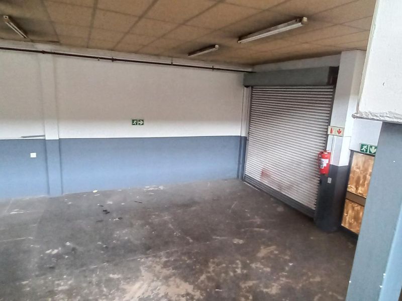 Spacious industrial garage area featuring a roller shutter door, concrete flooring, and functional overhead lighting, suitable for storage or workshop use.