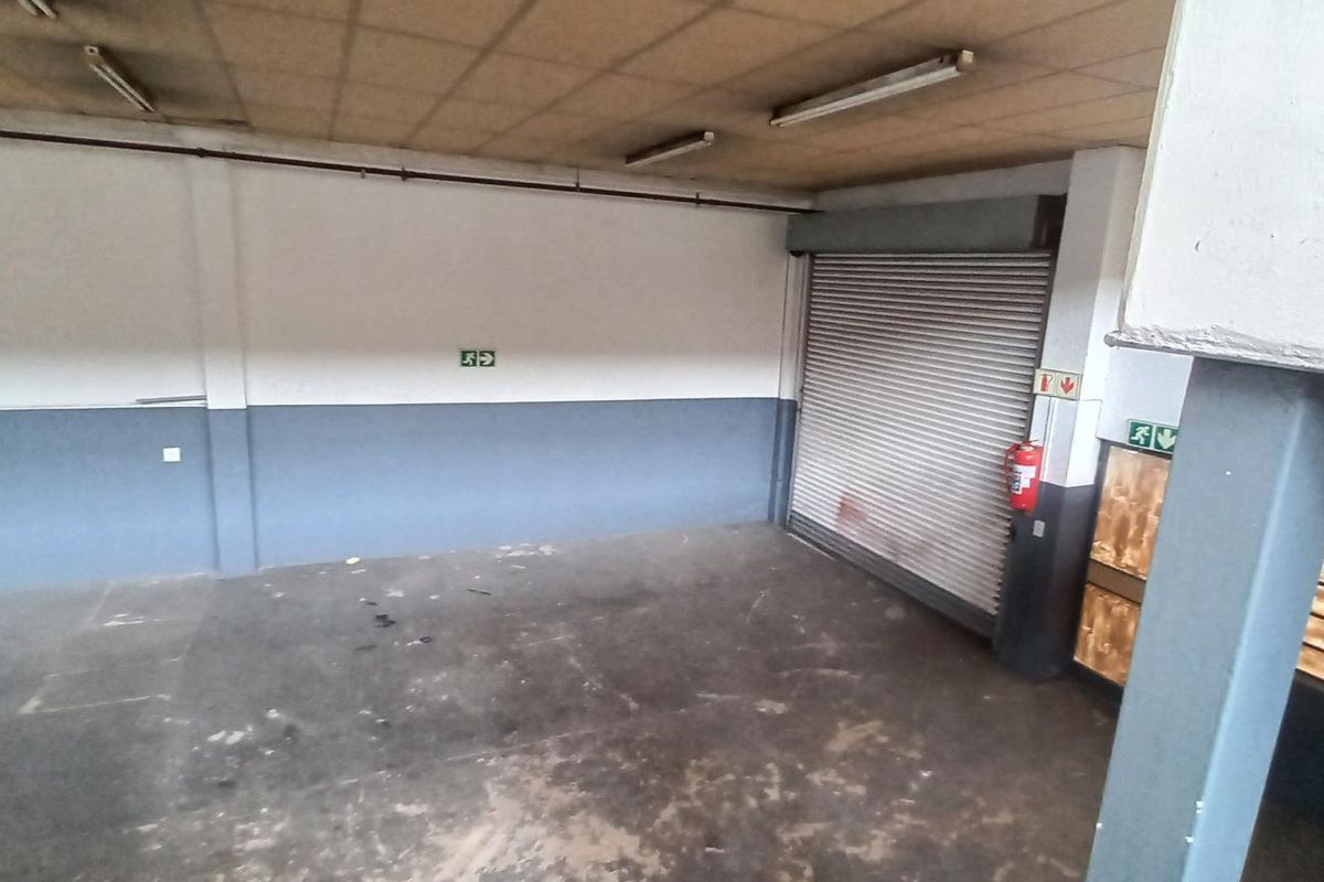 Spacious industrial garage area featuring a roller shutter door, concrete flooring, and functional overhead lighting, suitable for storage or workshop use.