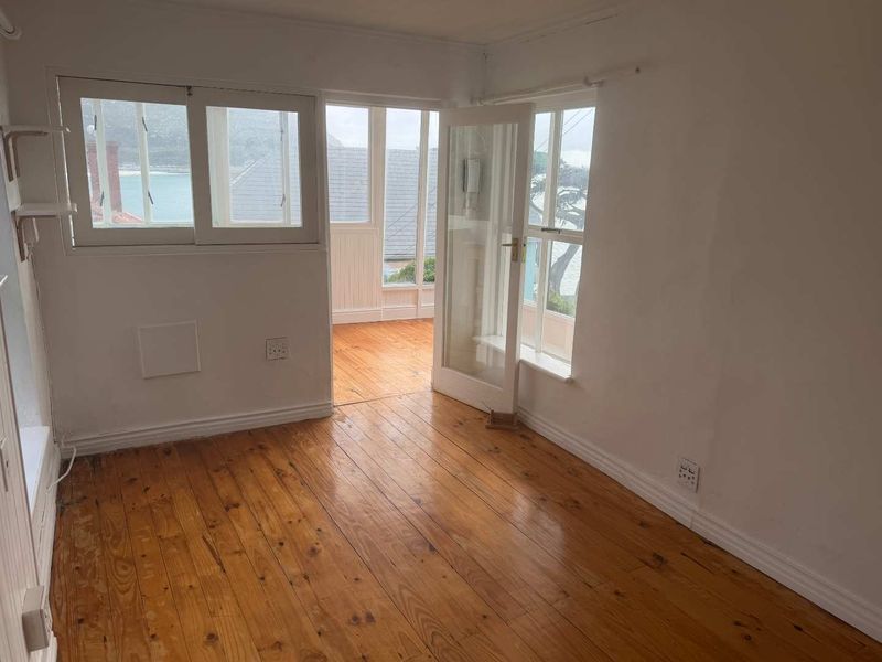 An empty bedroom featuring polished timber flooring, classic french doors leading to an enclosed balcony, and ample natural light.