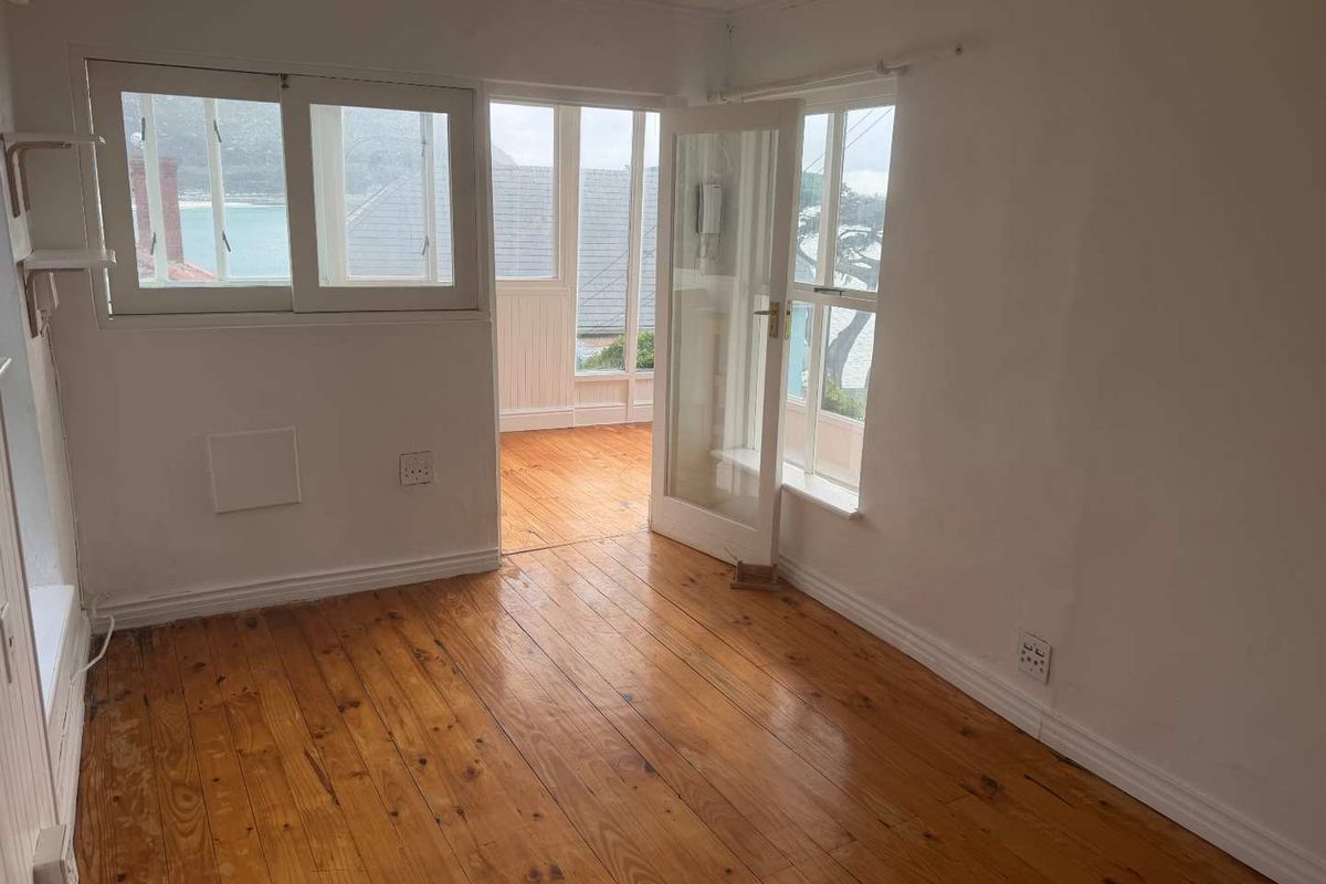 An empty bedroom featuring polished timber flooring, classic french doors leading to an enclosed balcony, and ample natural light.