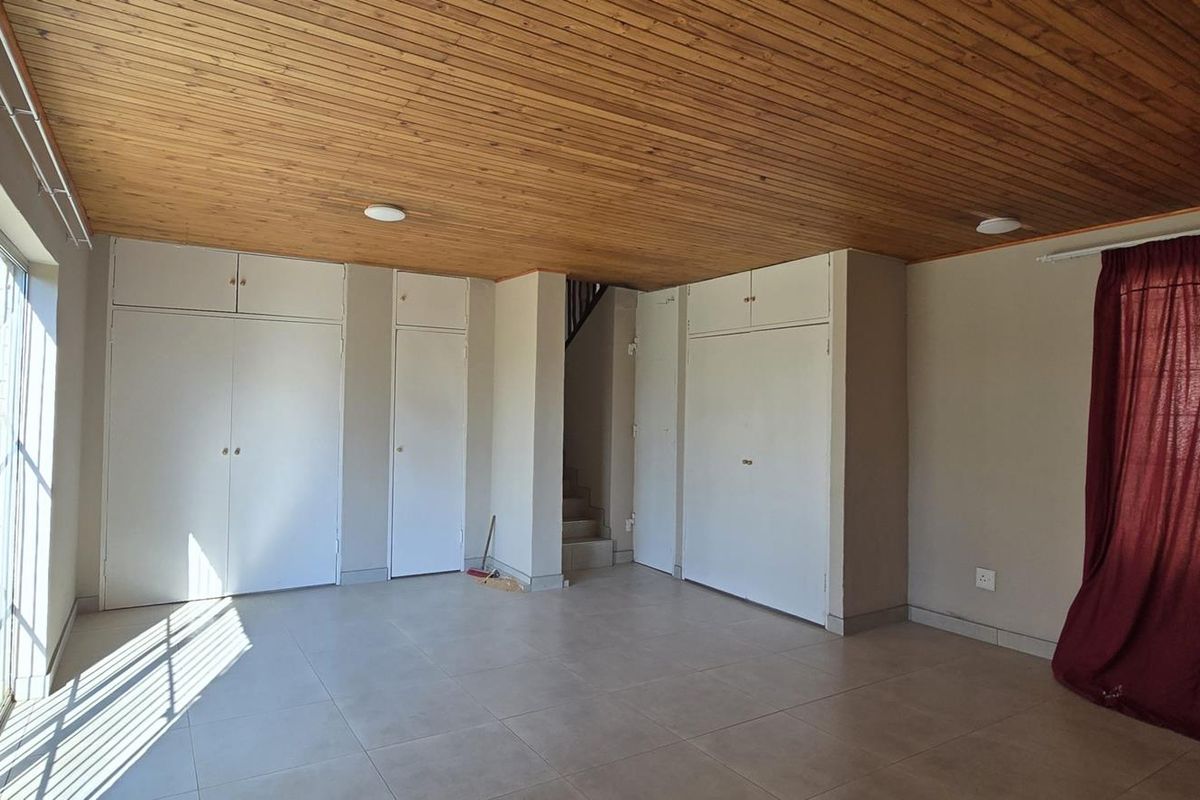 Spacious living area featuring a timber-clad ceiling, tiled flooring, and extensive built-in storage cupboards, with direct access to an outdoor area.