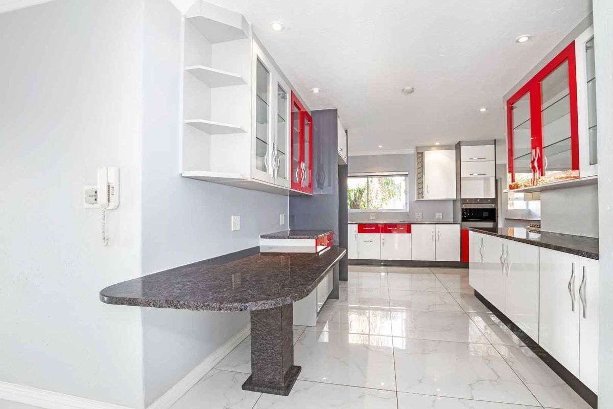 Modern kitchen featuring high-gloss cabinetry, granite countertops, a breakfast bar, and tiled flooring with integrated built-in oven and cabinetry.