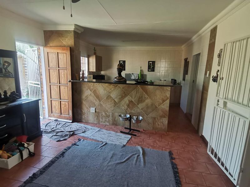 Open plan living and kitchen area featuring a tiled breakfast bar, terracotta floor tiles, and direct access to the exterior via a security gate.