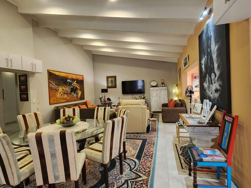 Spacious open-plan living and dining area featuring high vaulted ceilings with exposed beams and neutral tiled flooring throughout.