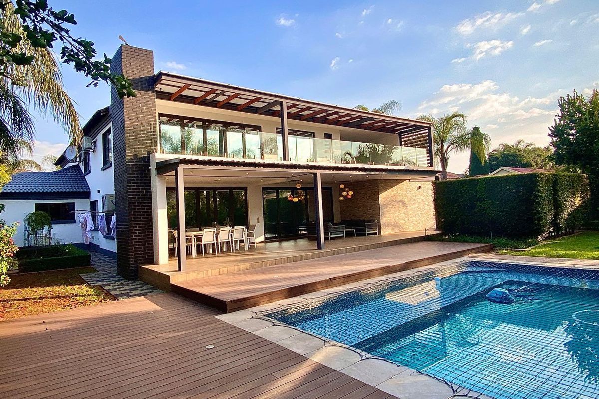 Spacious rear exterior featuring a large wooden deck, swimming pool with safety net, and a covered patio area with glass balustrades.