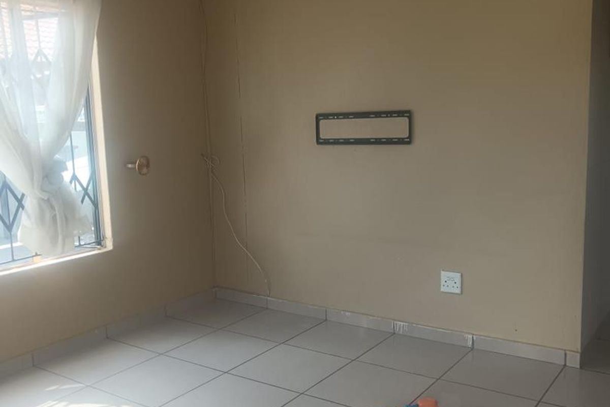 A simple living room featuring neutral wall tones, tiled flooring, and a wall-mounted television bracket.