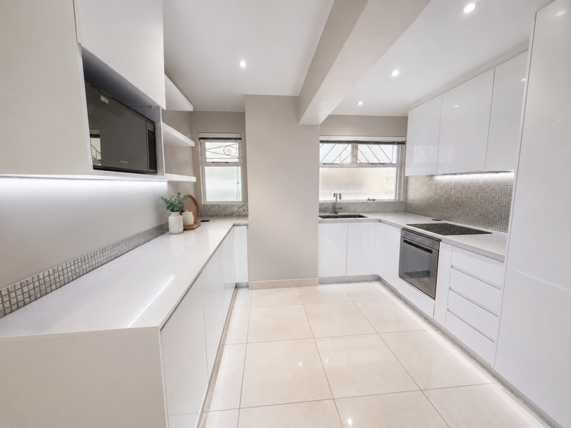 Modern, well-lit kitchen featuring sleek white gloss cabinetry, stone countertops, integrated appliances, and a stylish tiled backsplash.