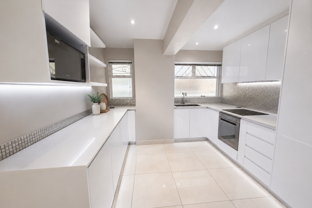 Modern, well-lit kitchen featuring sleek white gloss cabinetry, stone countertops, integrated appliances, and a stylish tiled backsplash.
