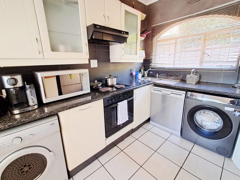 Functional kitchen featuring granite countertops, built-in cabinetry, integrated oven and hob, and tiled flooring with an arched window providing natural light.