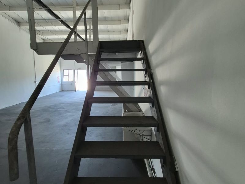 Industrial utility space featuring a metal staircase leading to a mezzanine level, exposed steel roof trusses, and durable concrete flooring.