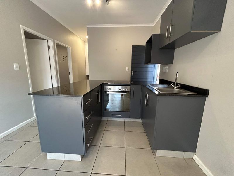 Modern kitchen featuring dark grey cabinetry, granite countertops, built-in oven and hob, and tiled flooring in an open-plan layout.