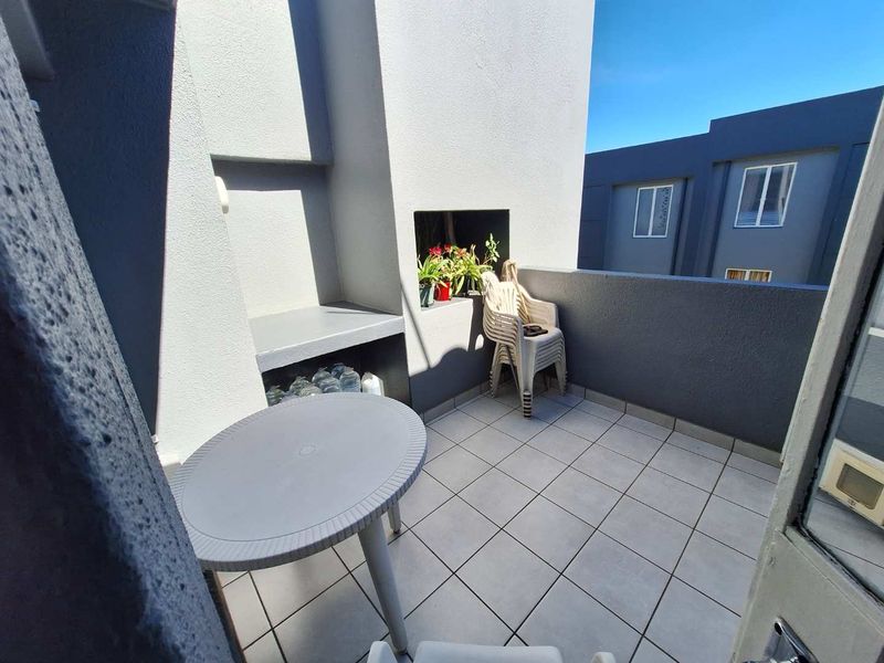 A compact balcony featuring tiled flooring and a built-in braai area, offering a functional outdoor space for relaxation.