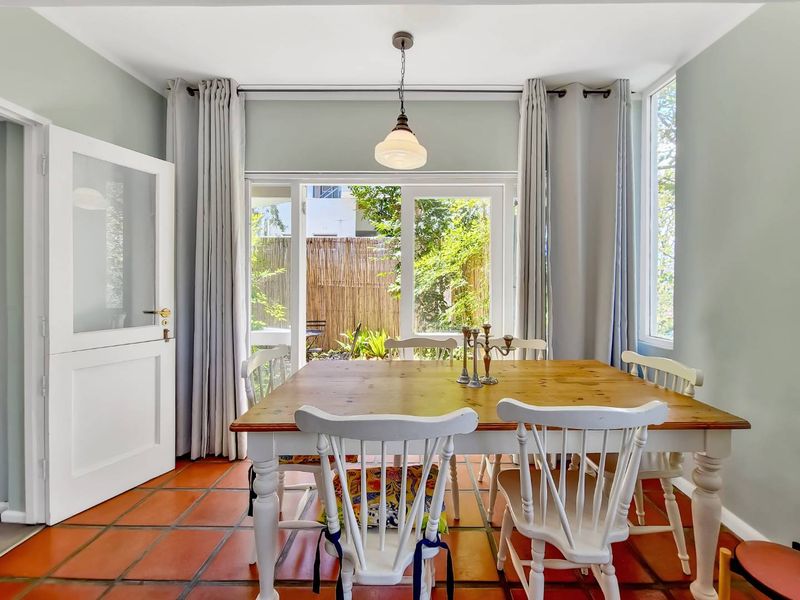 A bright dining room featuring terracotta floor tiles, a central pendant light, and direct access to the garden through glass french doors.