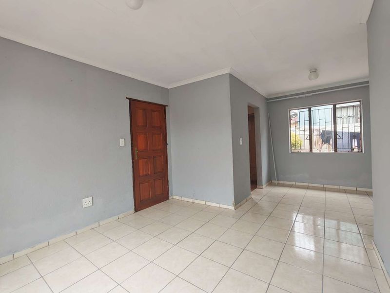 An empty living area featuring neutral grey walls, tiled flooring, and a timber door, providing a blank canvas for interior design.