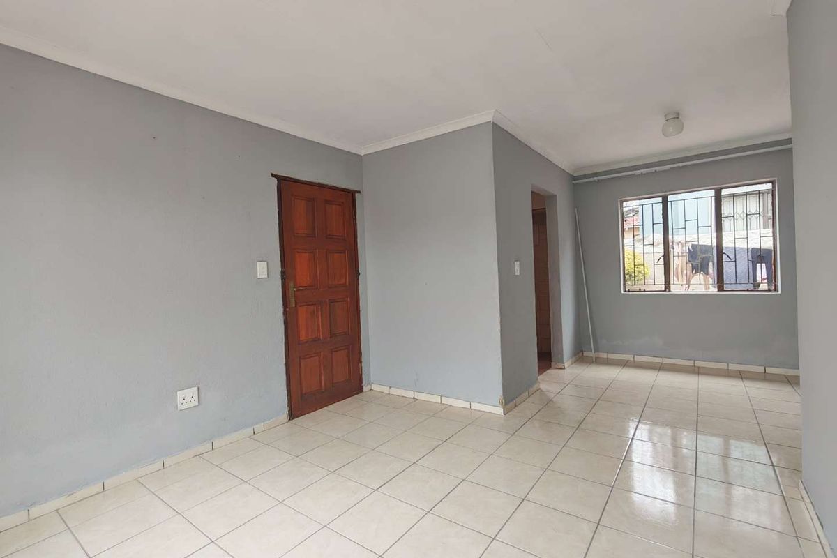 An empty living area featuring neutral grey walls, tiled flooring, and a timber door, providing a blank canvas for interior design.