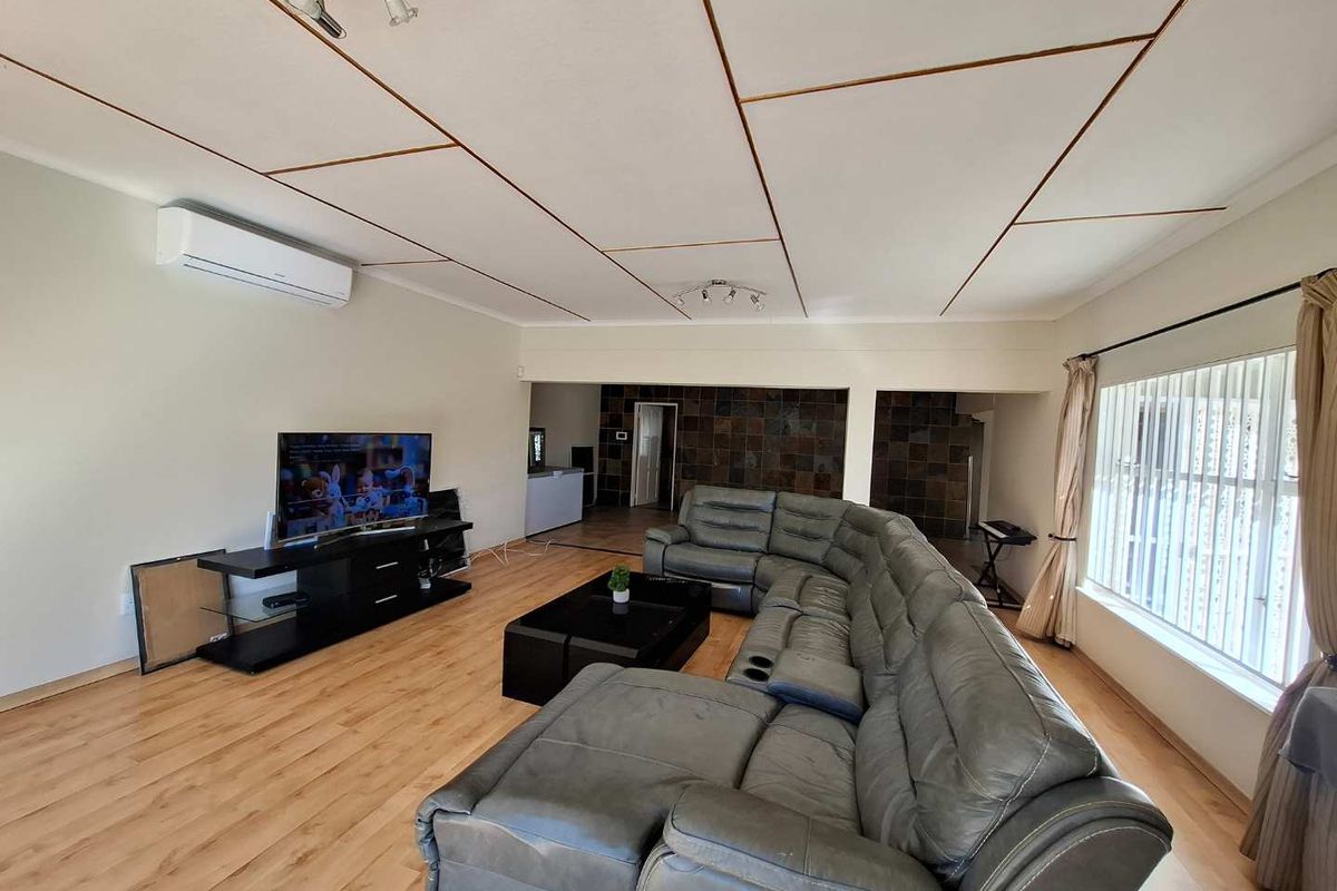 Spacious living room featuring laminate flooring, a split-system air conditioner, and a distinctive tiled feature wall in the adjoining area.