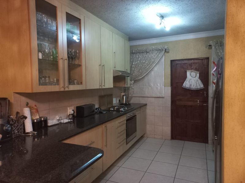 A functional kitchen featuring light wood cabinetry, granite countertops, built-in oven, hob, and extractor fan, with tiled flooring and a rear access door.