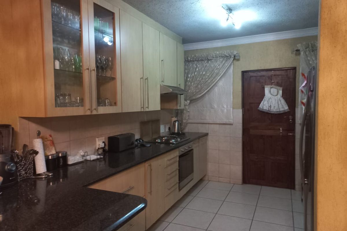 A functional kitchen featuring light wood cabinetry, granite countertops, built-in oven, hob, and extractor fan, with tiled flooring and a rear access door.