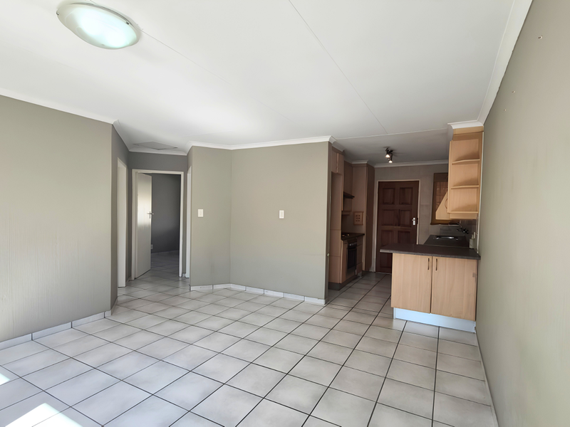 An open-plan living and kitchen area featuring neutral wall tones, tiled flooring, and functional built-in cabinetry with integrated oven.