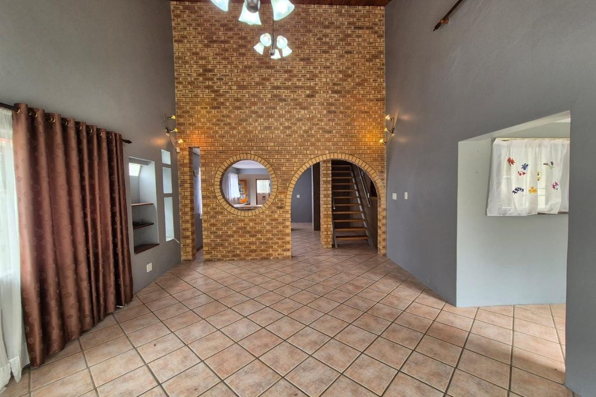 Spacious living area featuring a double-volume exposed brick wall, arched architectural details, timber ceiling, and tiled flooring, offering a unique character-filled layout.