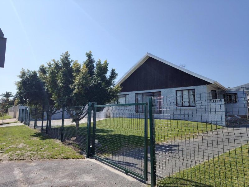 Front view of a single-story house featuring a brick facade, gabled roof, and a secure mesh perimeter fence with a sliding gate.