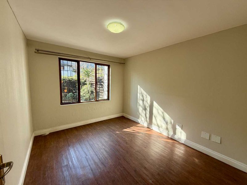 A bright, empty bedroom featuring laminate flooring, neutral walls, and a window fitted with security bars.