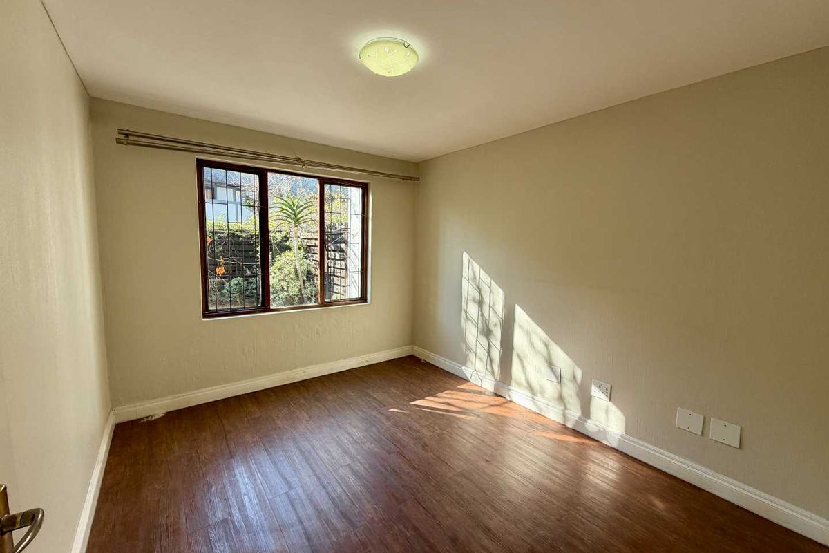 A bright, empty bedroom featuring laminate flooring, neutral walls, and a window fitted with security bars.