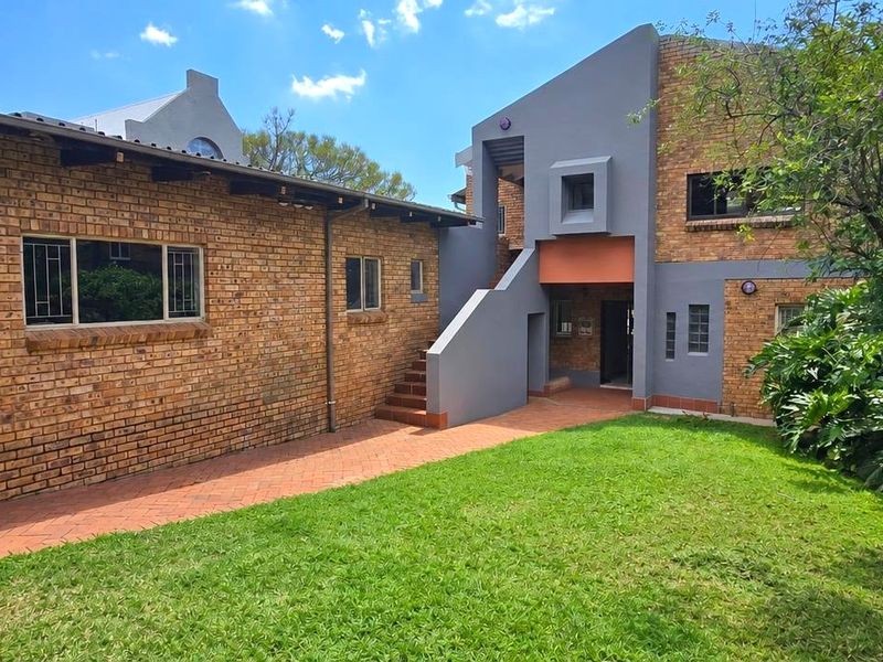 Rear view of the property featuring a brick facade, concrete staircase, paved walkway, and a well-maintained garden area.