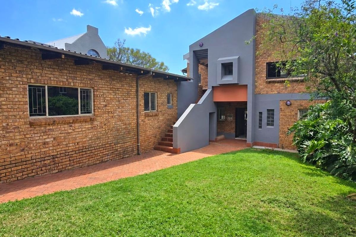 Rear view of the property featuring a brick facade, concrete staircase, paved walkway, and a well-maintained garden area.