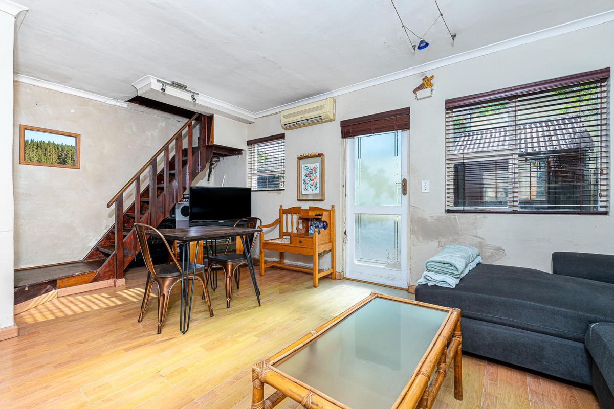 Open-plan living area featuring laminate flooring, a wooden staircase, and split-system air conditioning, requiring cosmetic updates to the wall finishes.