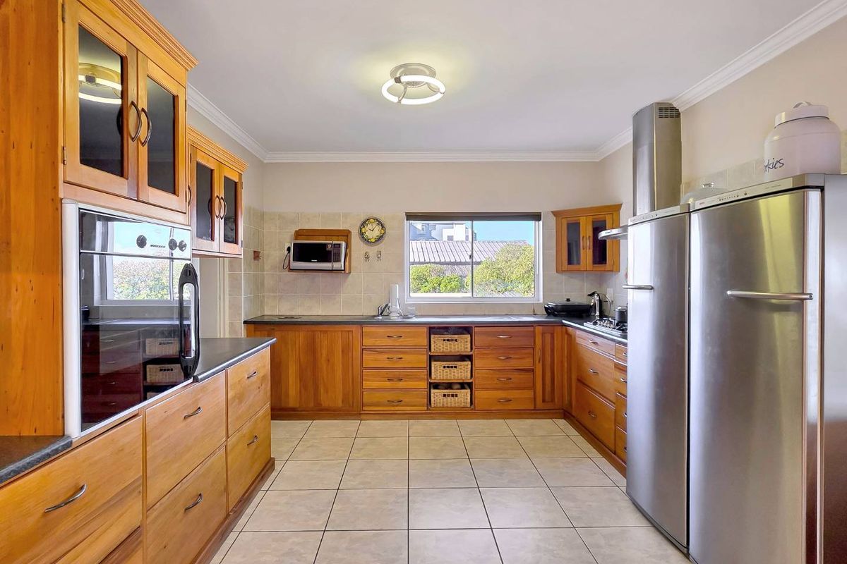 A functional kitchen featuring warm timber cabinetry, dark countertops, tiled flooring, and stainless steel appliances including a built-in oven and extractor fan.
